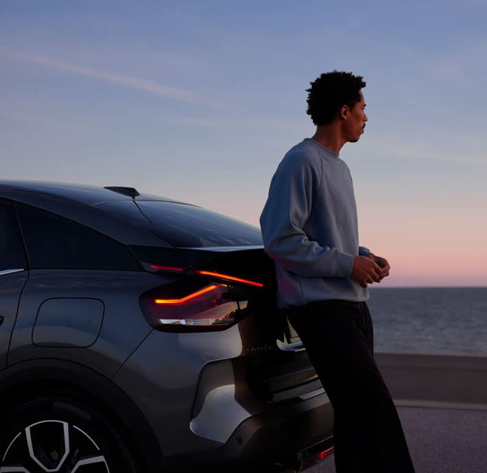 jeune homme assis contre voiture citroen C4 regardant l'horizon au bord de la mer